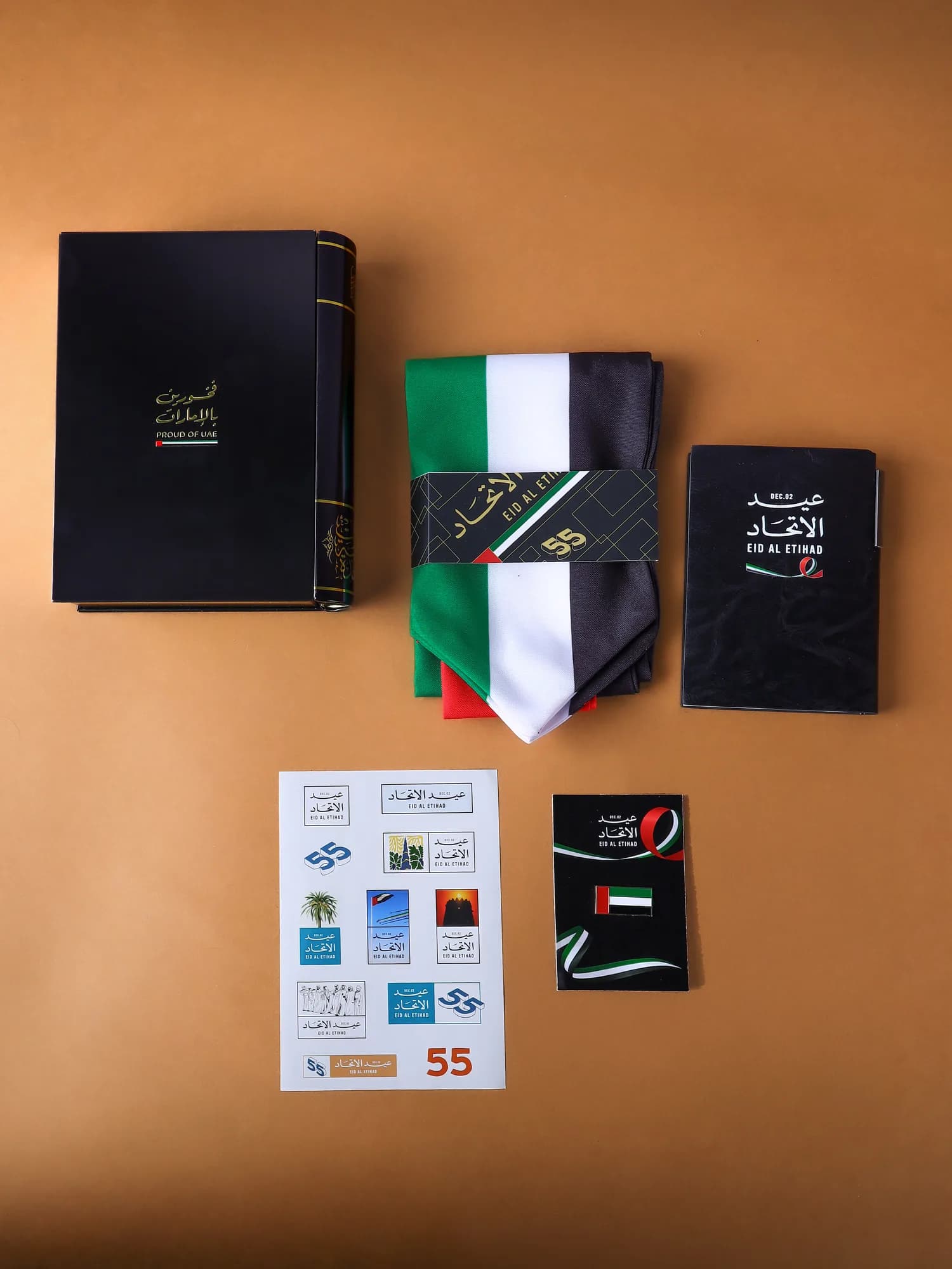 The gift laid out: the metal book, the flag scarf with its Eid Al Etihad 55 band, the notebook, the sticker sheet and the pin card